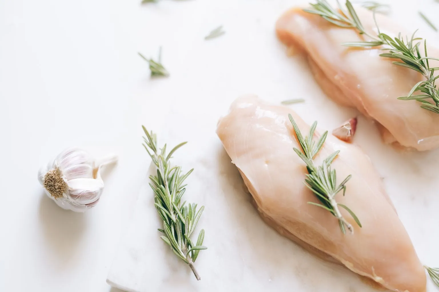 Pechugas de pollo crudas sobre una superficie de mármol con romero y ajo